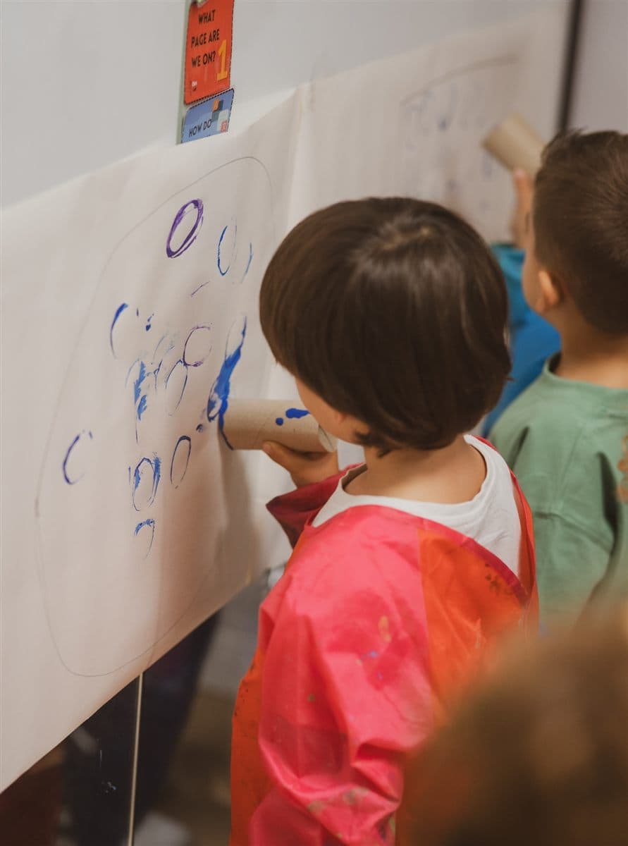 Peques pintando círculos con tubos de cartón en un taller